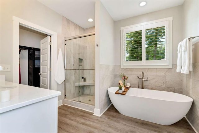 bathroom with vanity, wood-type flooring, tile walls, and plus walk in shower