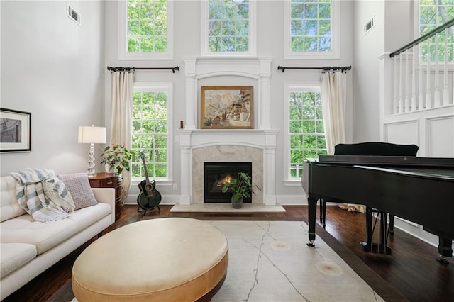 sitting room featuring visible vents, a towering ceiling, wood finished floors, and a premium fireplace
