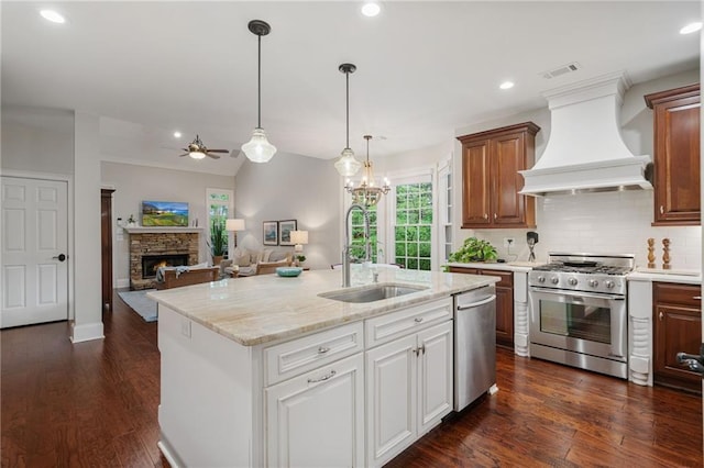 kitchen with a sink, custom exhaust hood, a fireplace, a ceiling fan, and appliances with stainless steel finishes
