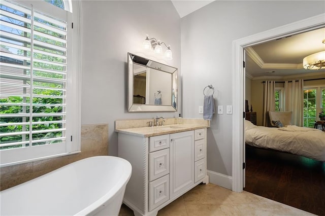 ensuite bathroom featuring vanity, ornamental molding, a raised ceiling, a freestanding bath, and tile patterned floors