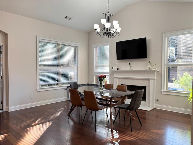 dining room featuring lofted ceiling, dark hardwood / wood-style flooring, a chandelier, and a premium fireplace