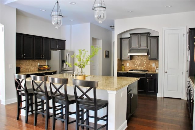 kitchen featuring appliances with stainless steel finishes, pendant lighting, an island with sink, a breakfast bar area, and dark hardwood / wood-style flooring