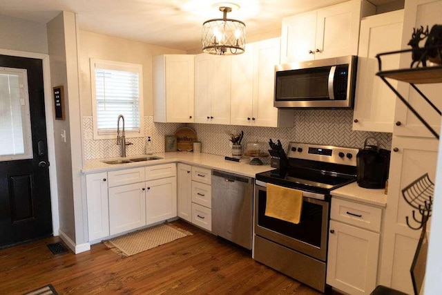 kitchen featuring pendant lighting, dark wood-type flooring, sink, appliances with stainless steel finishes, and white cabinetry