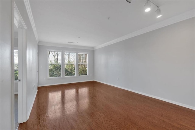 empty room featuring dark hardwood / wood-style flooring, crown molding, and rail lighting