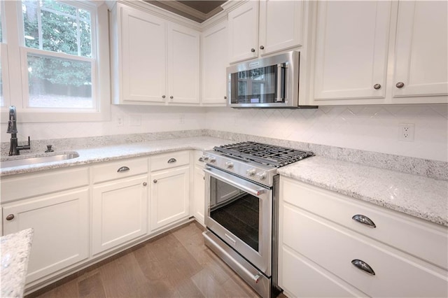 kitchen with light stone counters, stainless steel appliances, sink, light hardwood / wood-style flooring, and white cabinetry