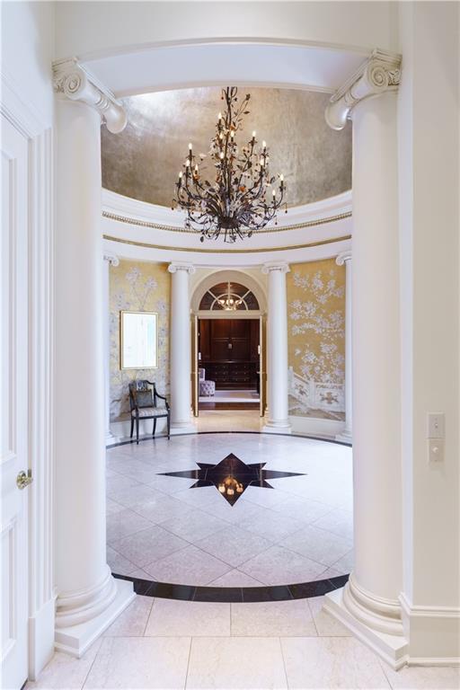 hallway with a notable chandelier, tile patterned floors, and decorative columns