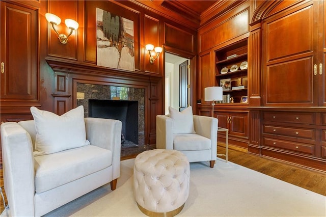 sitting room featuring hardwood / wood-style flooring, wooden walls, a fireplace, ornamental molding, and built in shelves