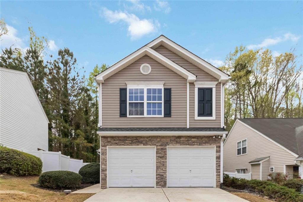 view of front of property with fence, an attached garage, stone siding, and concrete driveway