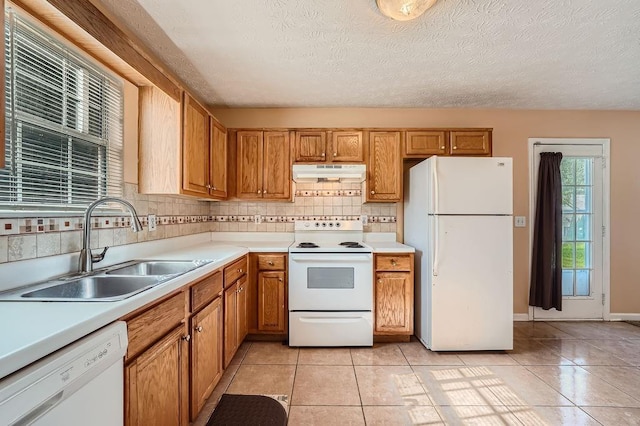 kitchen featuring white appliances, light countertops, under cabinet range hood, a sink, and light tile patterned floors