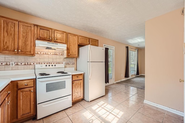 kitchen featuring white appliances, brown cabinetry, decorative backsplash, light tile patterned floors, and under cabinet range hood