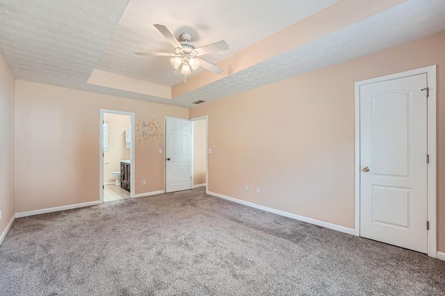 unfurnished bedroom with carpet floors, baseboards, ensuite bathroom, and a raised ceiling