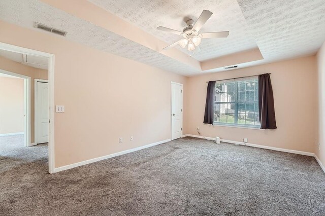 spare room featuring a textured ceiling, visible vents, baseboards, a raised ceiling, and carpet flooring