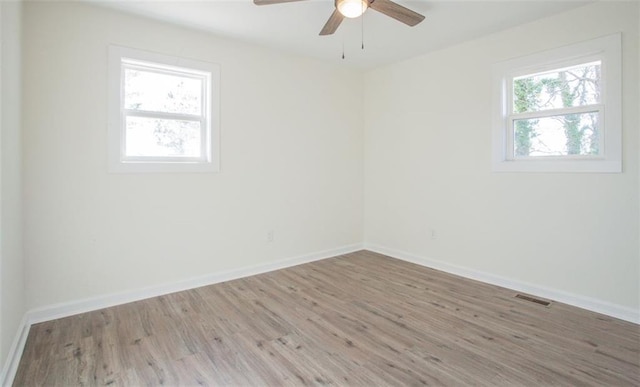 empty room with visible vents, a healthy amount of sunlight, baseboards, and wood finished floors