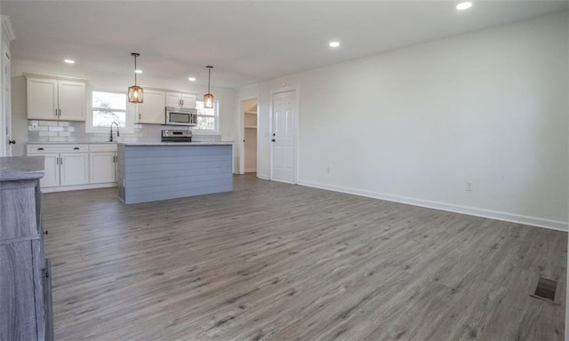 kitchen featuring light wood-style flooring, a sink, stainless steel appliances, white cabinets, and open floor plan