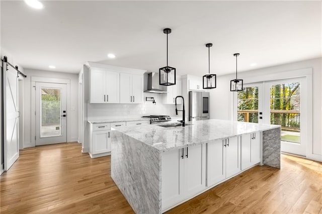 kitchen with a kitchen island with sink, white cabinets, and wall chimney exhaust hood