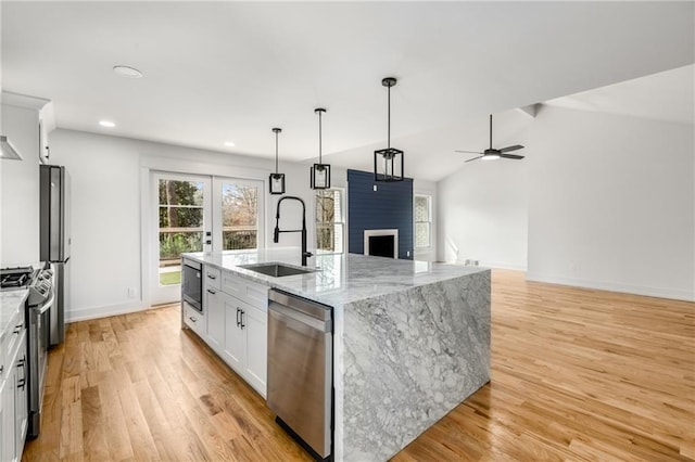 kitchen with sink, appliances with stainless steel finishes, light stone counters, white cabinets, and a center island with sink