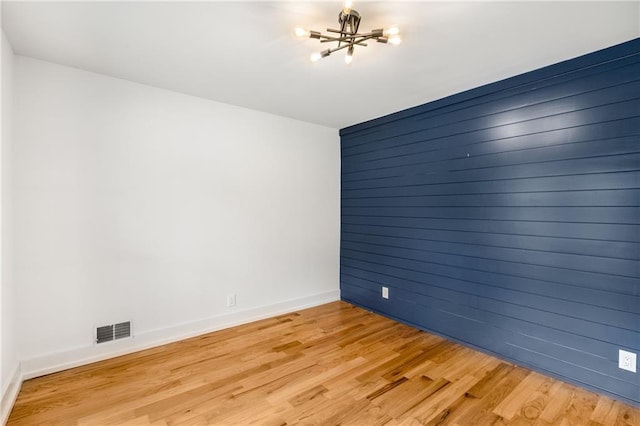 unfurnished room with a notable chandelier and light wood-type flooring