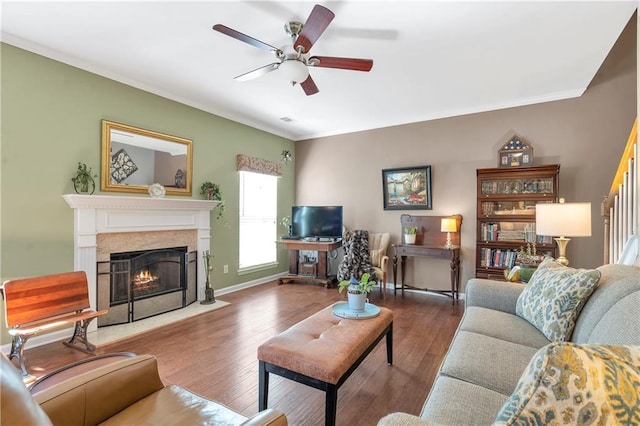 living area featuring a ceiling fan, wood finished floors, baseboards, a high end fireplace, and crown molding