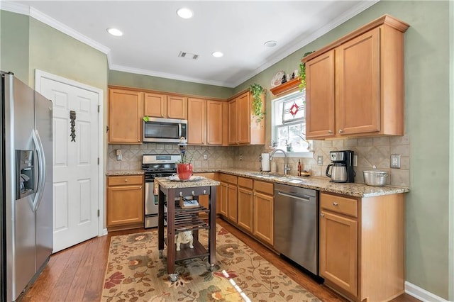 kitchen with wood finished floors, visible vents, ornamental molding, a sink, and appliances with stainless steel finishes