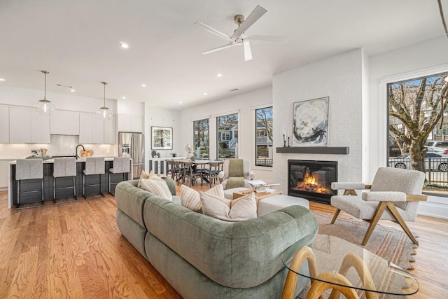 living room with a ceiling fan, a brick fireplace, light wood-style flooring, and recessed lighting