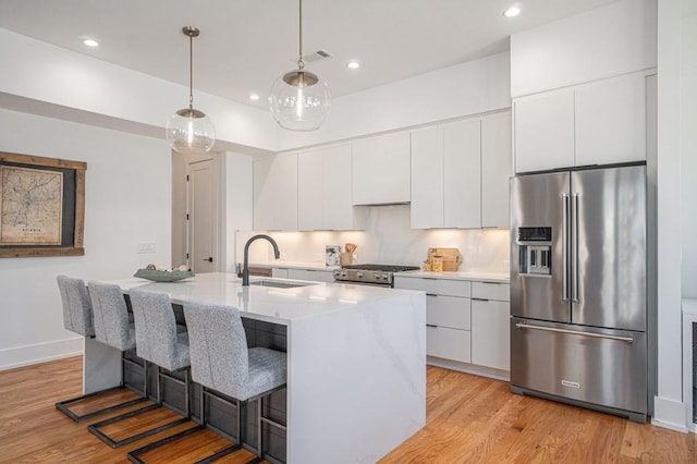 kitchen featuring light wood finished floors, light countertops, appliances with stainless steel finishes, white cabinetry, and a sink