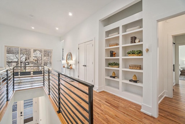 hall with light wood finished floors, built in shelves, and an upstairs landing