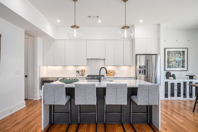 kitchen featuring high end fridge, light countertops, a sink, and light wood finished floors