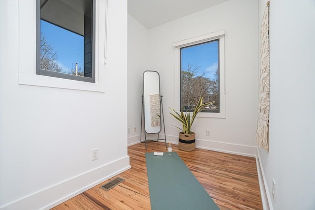 workout area with baseboards, visible vents, and wood finished floors