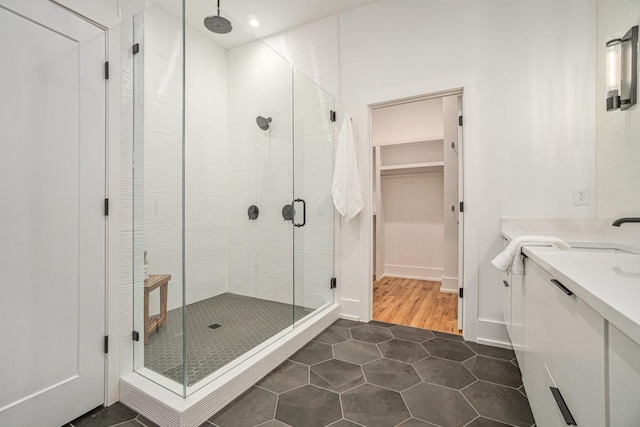 full bathroom featuring a stall shower, vanity, a walk in closet, and tile patterned floors