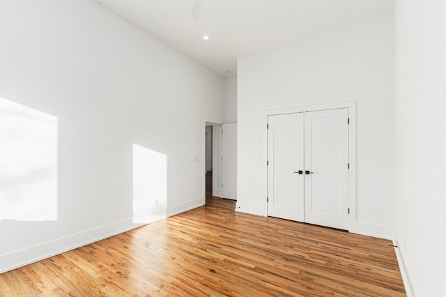 unfurnished bedroom with recessed lighting, a high ceiling, light wood-style flooring, and baseboards