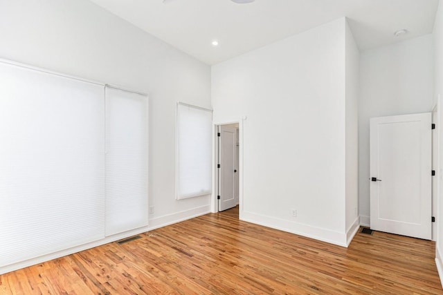 empty room featuring light wood-style flooring, recessed lighting, a high ceiling, visible vents, and baseboards