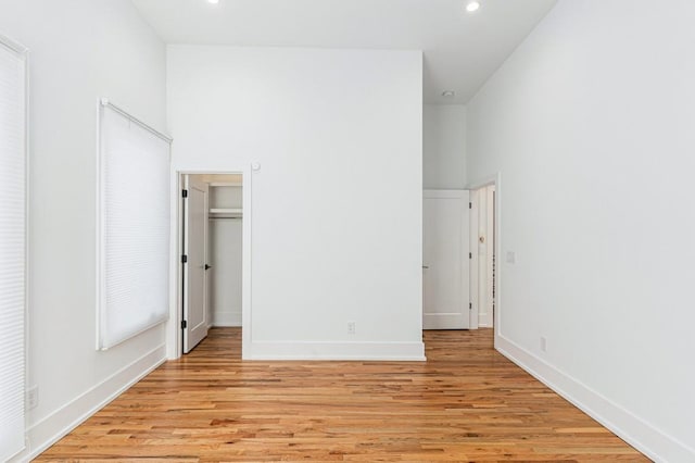 unfurnished bedroom with light wood-type flooring, a towering ceiling, baseboards, and recessed lighting