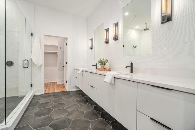 bathroom featuring tile patterned flooring, a sink, a spacious closet, double vanity, and a stall shower