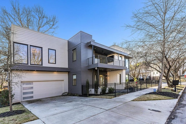 modern home with concrete driveway, an attached garage, fence, and a balcony