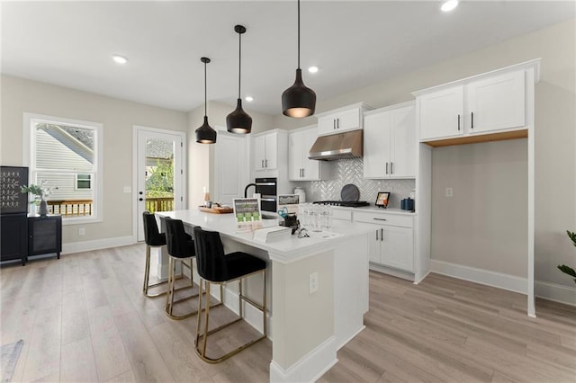 1941 Quarry Park Pl NW, Atlanta, GA 30318 - kitchen featuring under cabinet range hood, light wood-style floors, baseboards, an island with sink, and white cabinets