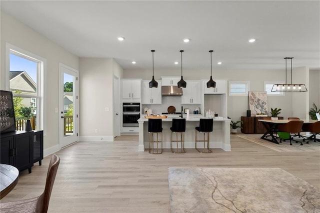 1941 Quarry Park Pl NW, Atlanta, GA 30318 - kitchen featuring under cabinet range hood, white cabinetry, light countertops, a kitchen island with sink, and light wood-style flooring