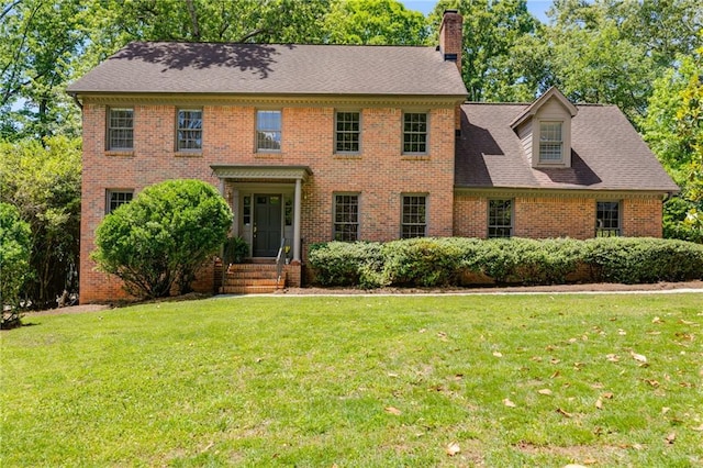 colonial house featuring a front lawn, brick siding, a chimney, and a shingled roof