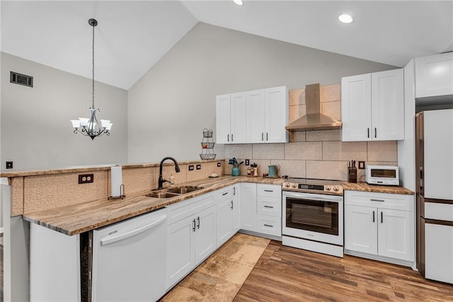 kitchen with sink, wall chimney range hood, white appliances, white cabinets, and kitchen peninsula