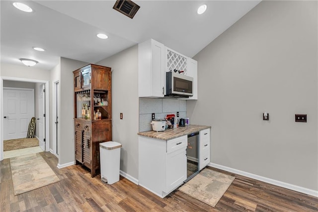 kitchen with tasteful backsplash, white cabinetry, wine cooler, hardwood / wood-style flooring, and light stone counters