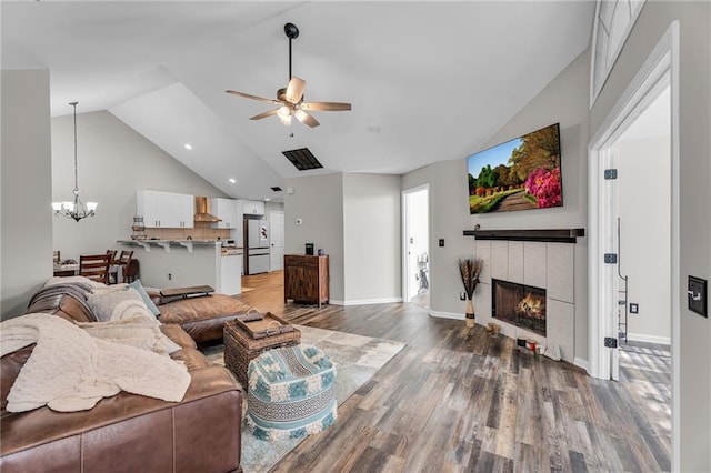 living room with high vaulted ceiling, ceiling fan with notable chandelier, wood-type flooring, and a tile fireplace