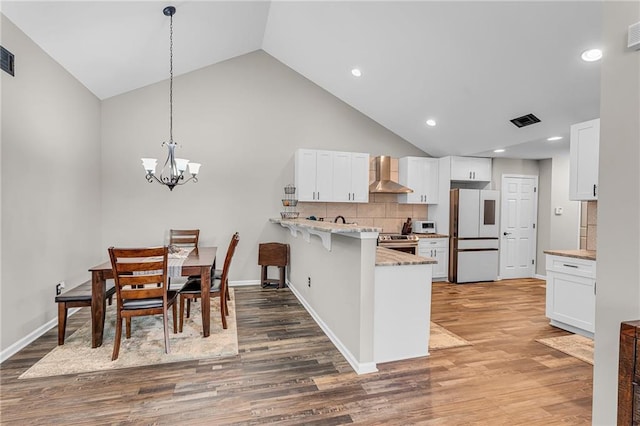 kitchen featuring refrigerator, decorative light fixtures, white cabinetry, a kitchen bar, and wall chimney exhaust hood