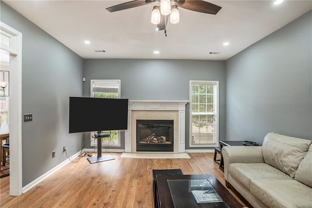 living room featuring ceiling fan, a premium fireplace, and light hardwood / wood-style flooring