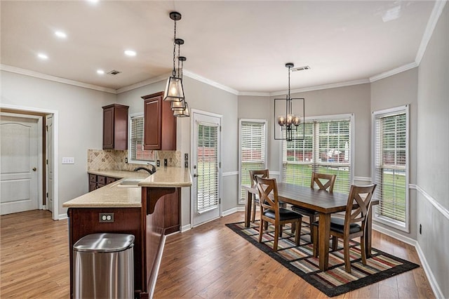 kitchen with crown molding, sink, decorative light fixtures, light hardwood / wood-style flooring, and a notable chandelier