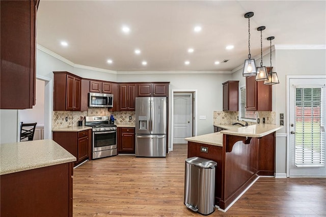 kitchen with kitchen peninsula, a kitchen breakfast bar, stainless steel appliances, light hardwood / wood-style floors, and hanging light fixtures