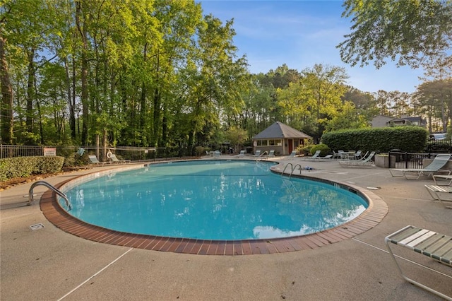 community pool with a patio, fence, and view of wooded area