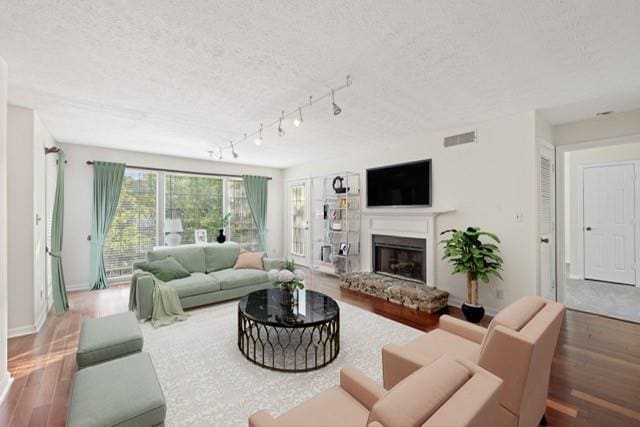 living room with wood finished floors, a textured ceiling, a fireplace with raised hearth, baseboards, and track lighting