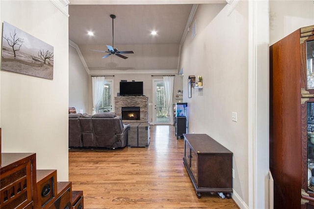 living area with ceiling fan, a stone fireplace, visible vents, ornamental molding, and light wood finished floors