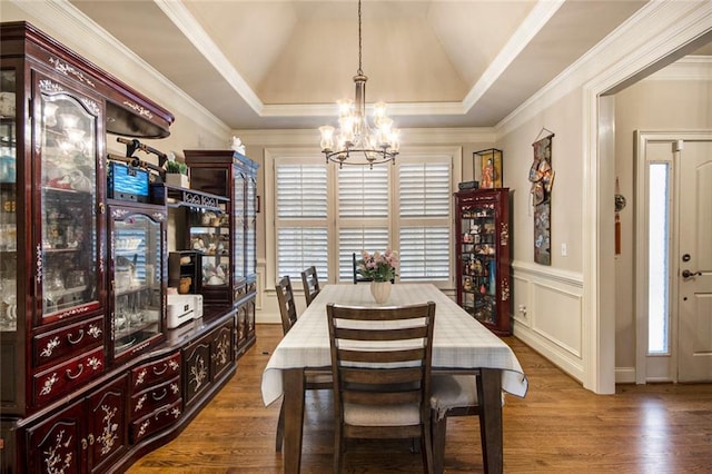 dining room featuring dark wood finished floors, a raised ceiling, an inviting chandelier, crown molding, and a decorative wall