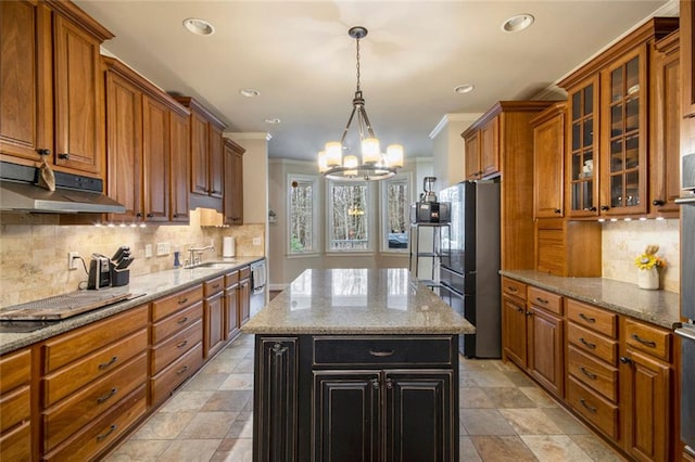 kitchen with cooktop, brown cabinetry, a kitchen island, light stone countertops, and under cabinet range hood