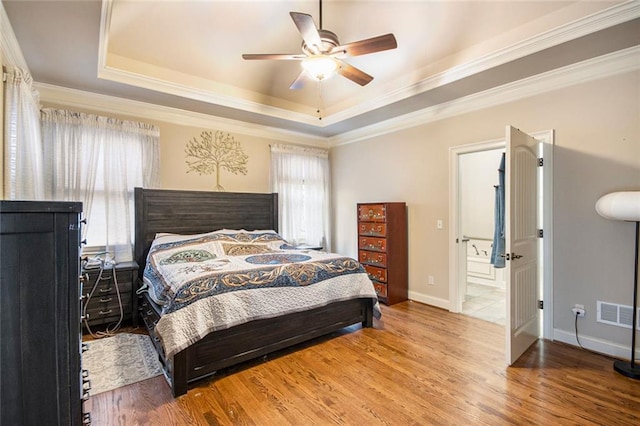 bedroom with a raised ceiling, crown molding, baseboards, and wood finished floors